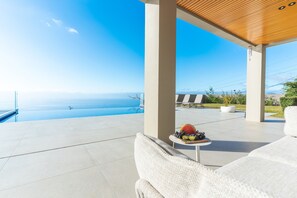 A modern outdoor seating area with a view of the ocean, a wooden ceiling, and a table with fruits. - Eco Monte by Atlantic Holiday (Funchal)