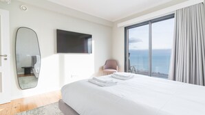 A modern hotel room with a large bed, a flat-screen TV, a large window with a view of the sea, and a chair by the window. - Eco Monte by Atlantic Holiday (Funchal)