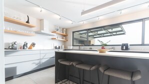 A modern kitchen with a large window, bar stools, and built-in shelves. - Eco Monte by Atlantic Holiday (Funchal)