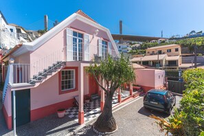 A pink building with a staircase, a tree in front, and a car parked nearby.