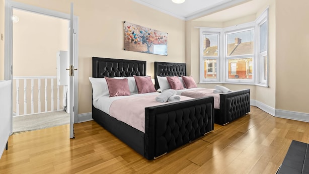 Una camera da letto con due testiere nere capitonate, un'ampia finestra con persiane bianche, un quadro di un albero e un pavimento in legno.