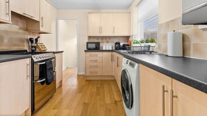 Una cucina moderna con mobili in legno, forno a incasso, microonde e lavatrice.