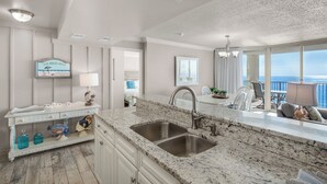 A modern kitchen with a large granite countertop, a double sink, and a view of the ocean through large windows. - Big August Discounts! Spacious 3BR Oceanfront Unit W/Free Beach Chair Service (Panama City Beach)