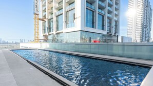 A modern building with a swimming pool, large windows, and a construction crane. - StayShort - 1BR in JVC that Sleeps 4 with a Balcony! (JVC)