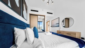 A modern hotel room with a large bed, a wooden nightstand, and a view of the city. - StayShort - 1BR in JVC that Sleeps 4 with a Balcony! (JVC)