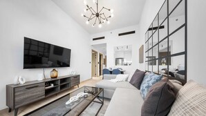 A modern living room with a flat-screen TV, a glass coffee table, a sofa, and a large mirror. - StayShort - 1BR in JVC that Sleeps 4 with a Balcony! (JVC)