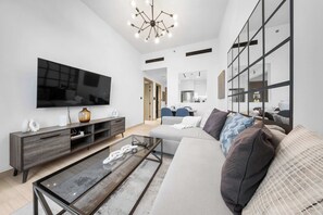 Ein modernes Wohnzimmer mit Fernseher, Glastisch, Sofa und einem großen Spiegel.