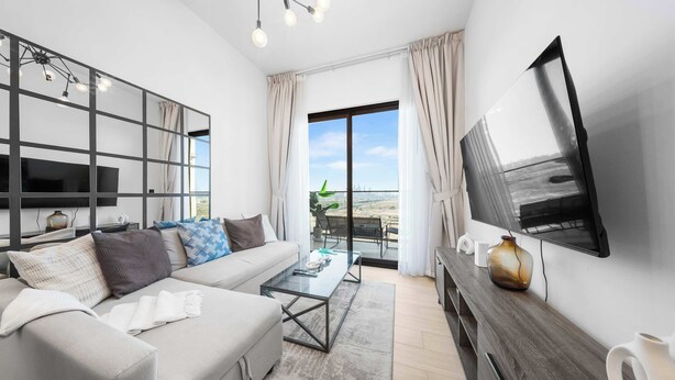A modern living room with a sofa, coffee table, and TV. - StayShort - 1BR in JVC that Sleeps 4 with a Balcony! (JVC)