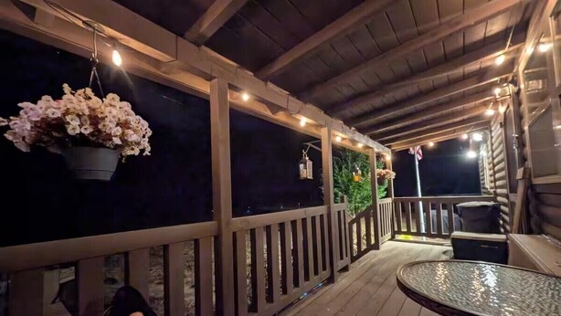 A wooden deck with a round table and chairs, a hanging flower arrangement, and a small Christmas tree. - Private 43-Acre Cabin Near Pinehurst with Trails, Pond, on property Sleeps 6 (Sanford)