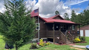 A cabin with a porch, a flag, and a small garden. - Private 43-Acre Cabin Near Pinehurst with Trails, Pond, on property Sleeps 6 (Sanford)