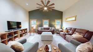 A spacious living room with a large ceiling fan, a television, and a wooden bookshelf. - Private 43-Acre Cabin Near Pinehurst with Trails, Pond, on property Sleeps 6 (Sanford)