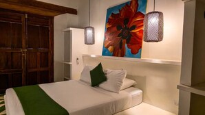 A bedroom with a bed, a green throw, a white headboard, a large floral painting, and two wall-mounted lamps. - Miskitu Granada - Boutique House in Colonial Center (Granada)