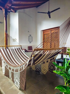 A hammock with a wooden frame and a woven seat, a ceiling fan, and a wooden door in a room with tiled flooring. - Miskitu: Colonial House with Pool in Granada's Historic Center (Granada)
