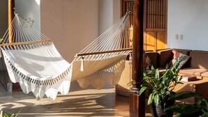 A hammock chair and a wicker sofa in a sunlit room with a tiled floor and a wooden door in the background. - Miskitu Granada - Boutique House in Colonial Center (Granada)