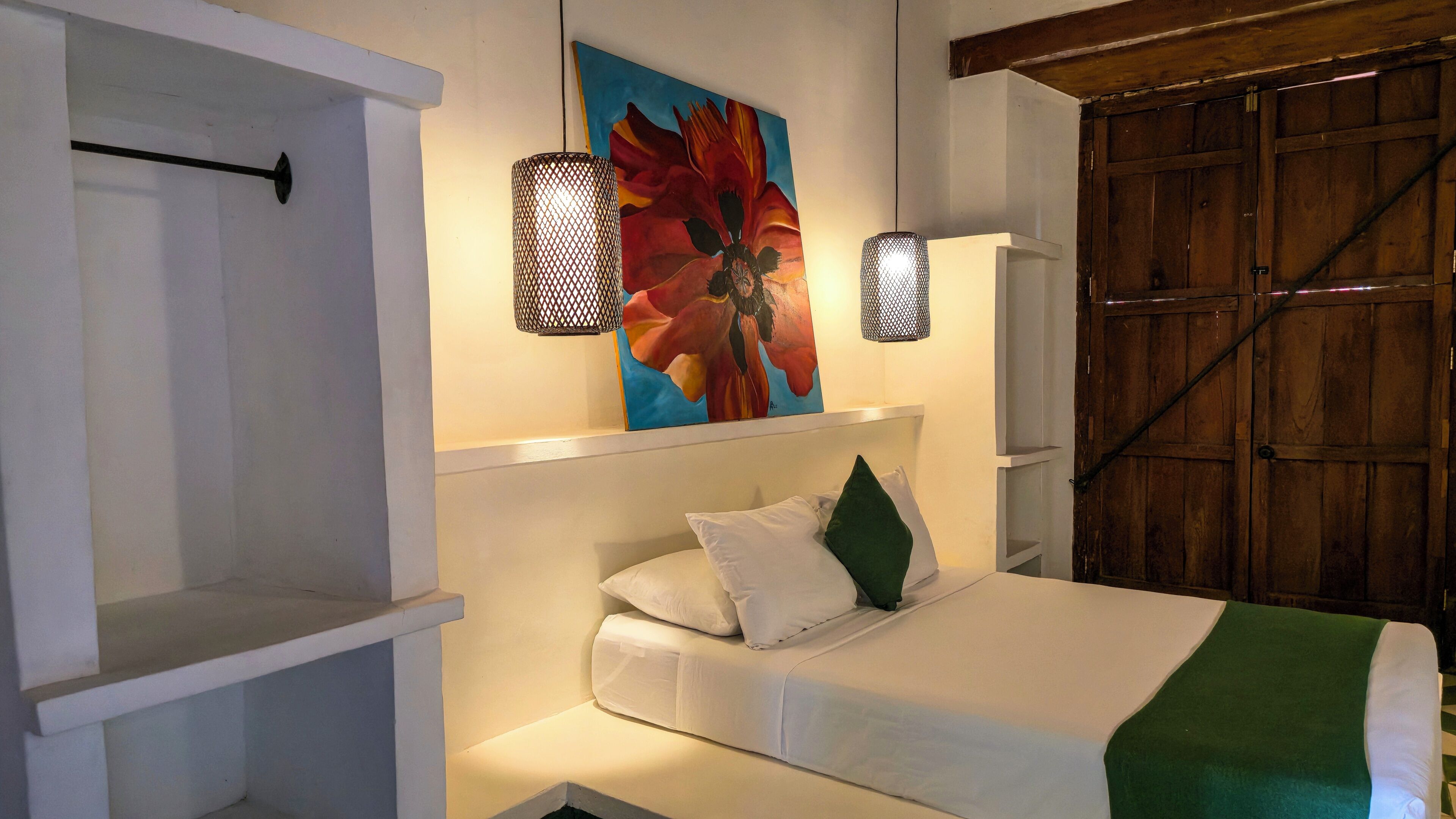 Een slaapkamer met een bed, een schilderij, twee wandlampen en een houten garderobe.