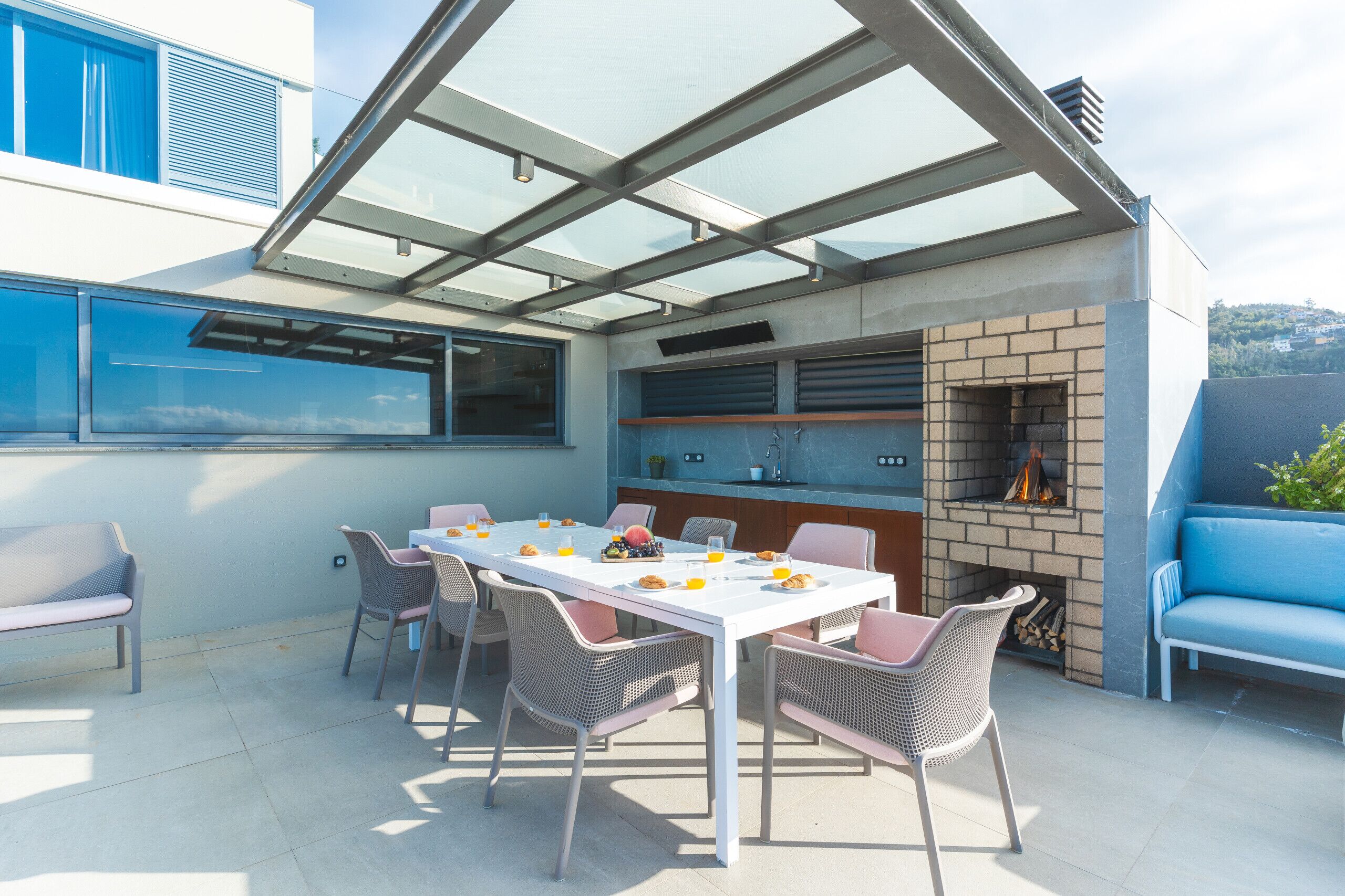 Un espace de repas extérieur moderne, doté d’un patio fermé par des baies vitrées, d’une cheminée en briques et d’un canapé bleu.