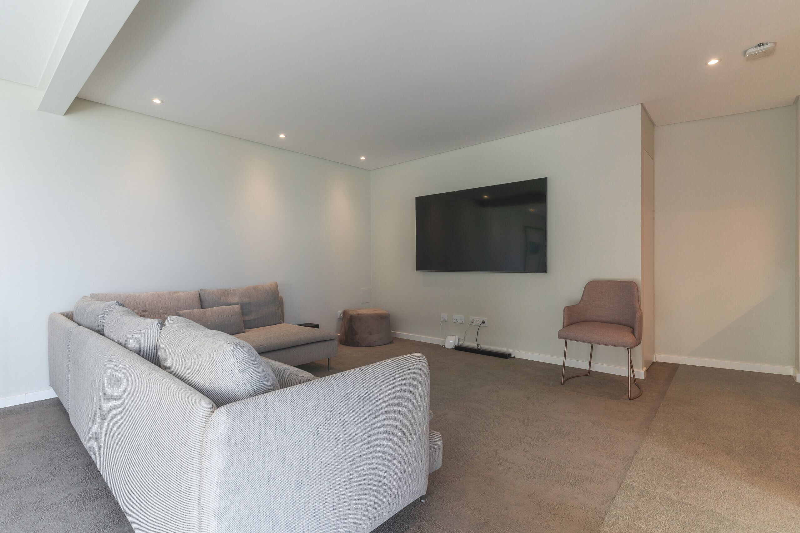 A modern living room with a sectional sofa, a single armchair, and a flat-screen TV mounted on the wall.