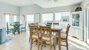 A dining area with a large table and chairs, a ceiling fan, and a view of the balcony. - Beachfront Beauty w/ Wraparound Deck & Private Dune Walkover (Galveston)