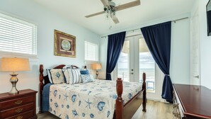 Une chambre à coucher avec un lit, des tables de chevet, un ventilateur de plafond et une vue sur l’extérieur.