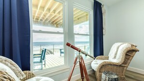 Une chambre avec vue sur la plage, un télescope, des meubles en osier et un tabouret à motifs.