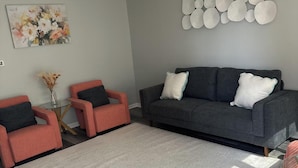 A modern living room with a grey sofa, two pink armchairs, a patterned rug, and a wall art piece. - Ranch Cozy Home close to O'Hare (River Grove)
