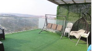 A balcony with artificial grass, a swing chair, a wicker chair, and a view of the countryside. - stunning appartment in jerusalem romema (Jerusalem)