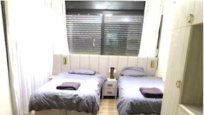 A bedroom with two beds, a window with blinds, a nightstand, and a wardrobe. - stunning appartment in jerusalem romema (Jerusalem)