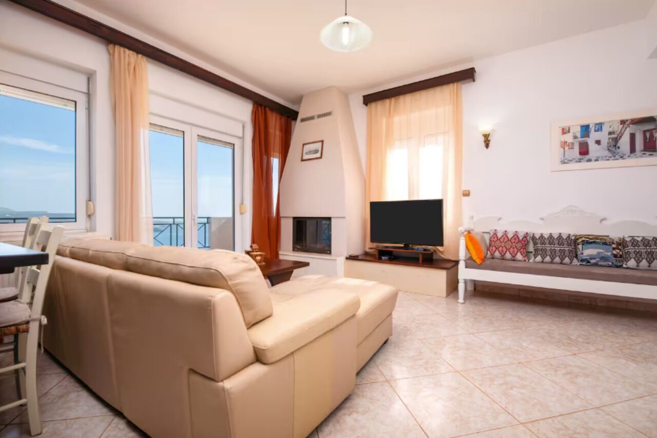 A living room with a beige sofa, a TV, and a balcony with curtains.