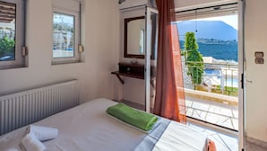 A hotel room with a bed, a window, a mirror, a radiator, and a view of the sea. - Aptera Dream Apartment (Souda)