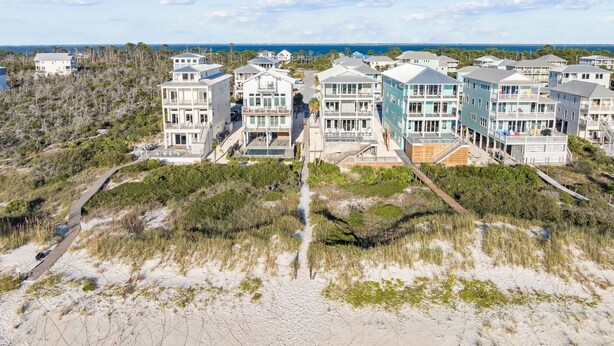 Un quartier résidentiel situé sur la côte, avec des maisons modernes à plusieurs étages, une plage de sable et une vue sur l’océan.