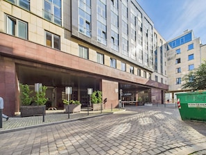 A modern hotel with a covered entrance, paved courtyard, and a green dumpster. - Wroclaw Rynek Citycenter Stay Galeria Dominikanska (Wrocław)