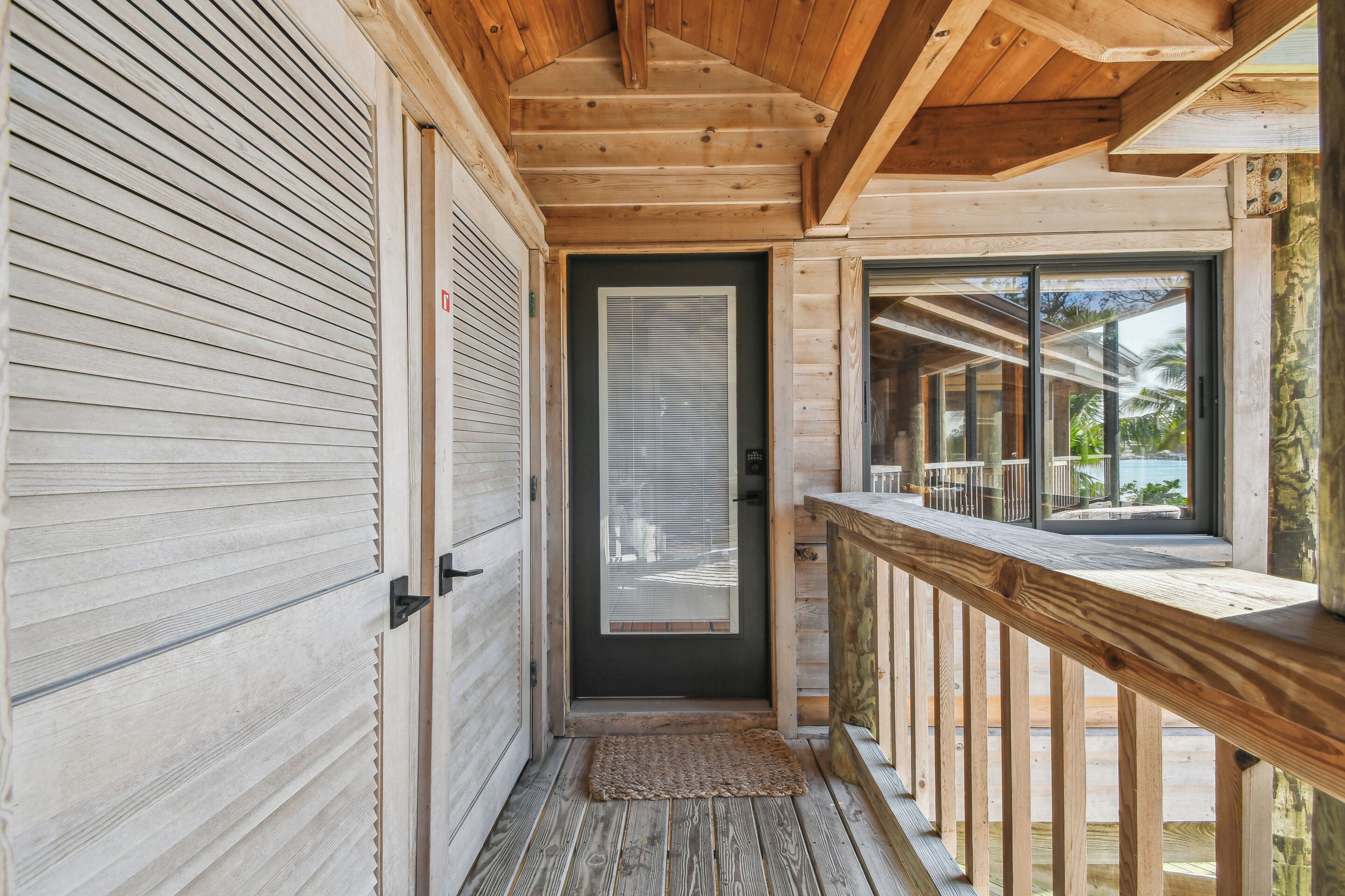 A wooden exterior with a sliding door, a small porch with a wooden railing, and a view of the outdoors.
