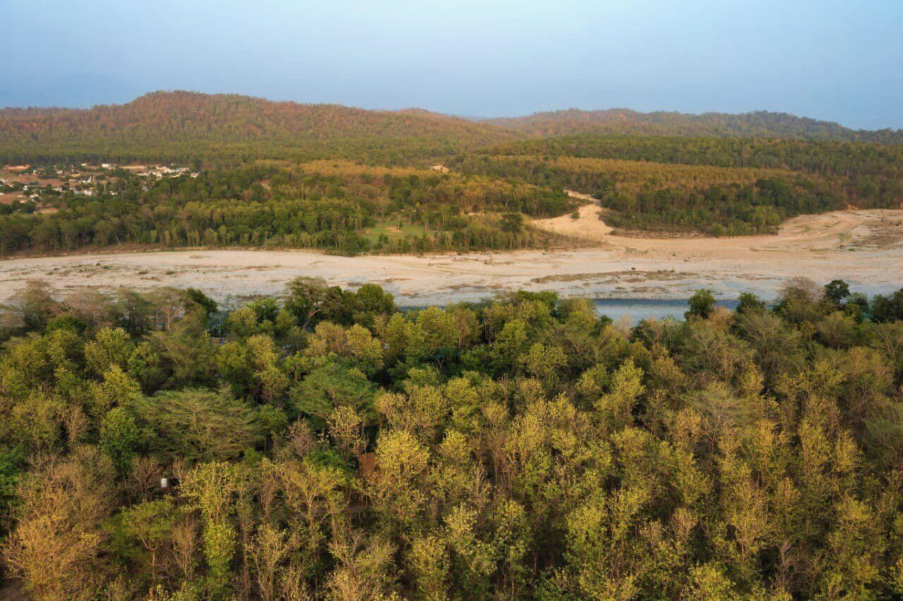 A natural landscape with a forested area, a river, and distant hills.
