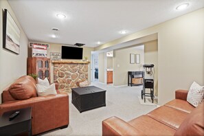 A spacious living area with leather sofas, a stone fireplace, and a television mounted on the wall. - Evergreen Grove | Hocking Hills, Hot Tub, Firepit (Sugar Grove)