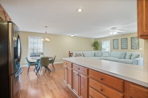 A modern kitchen with wooden cabinets, a large island, and a dining area with chairs and a table. - Evergreen Grove | Hocking Hills, Hot Tub, Firepit (Sugar Grove)