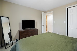 A bedroom with a bed, a dresser, a television, and a door leading to another room. - Evergreen Grove | Hocking Hills, Hot Tub, Firepit (Sugar Grove)