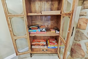 A wooden shelf unit with multiple compartments, some containing board games like Scrabble and Risk. - Evergreen Grove | Hocking Hills, Hot Tub, Firepit (Sugar Grove)