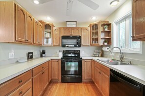 A kitchen with wooden cabinets, a black microwave, a stainless steel sink, and a dishwasher.