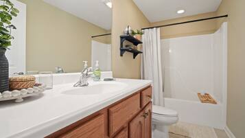 A bathroom with a white sink, wooden cabinets, a toilet, a shower with a curtain, and a mirror.