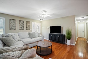 A living room with a gray sofa, a round coffee table, a black entertainment unit, and a ceiling fan. - Evergreen Grove | Hocking Hills, Hot Tub, Firepit (Sugar Grove)