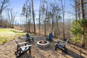 A fire pit surrounded by Adirondack chairs in a forested area. - Evergreen Grove | Hocking Hills, Hot Tub, Firepit (Sugar Grove)
