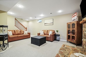 A living room with a brown leather sofa, a black coffee table, a stone accent wall, a wooden cabinet, and a staircase. - Evergreen Grove | Hocking Hills, Hot Tub, Firepit (Sugar Grove)