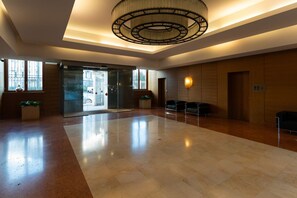 A spacious lobby with a modern chandelier, glass doors leading outside, and seating areas.