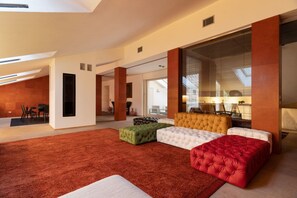 A modern interior with a large sectional sofa, a red ottoman, and a dining area with chairs.