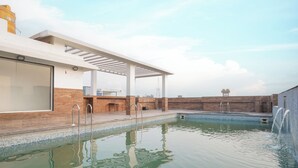 Una piscina con pérgola, fuente de agua y vista al cielo.