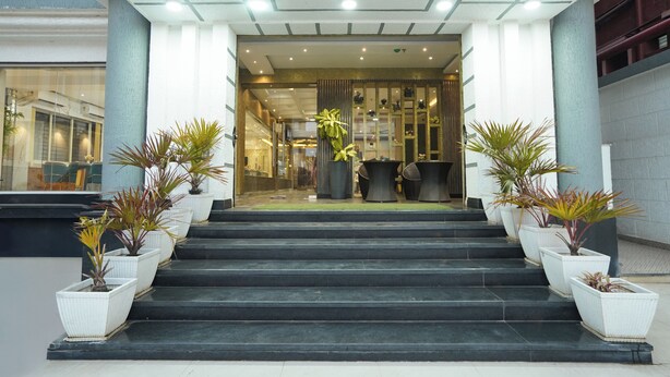 Entrada de hotel con una serie de escalones negros que conducen a una puerta de cristal. Hay plantas en macetas a ambos lados de la escalera.