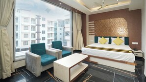 Un cuarto de hotel con un ventanal grande, una cama con cabecera, un escritorio, dos sillones y una mesita.