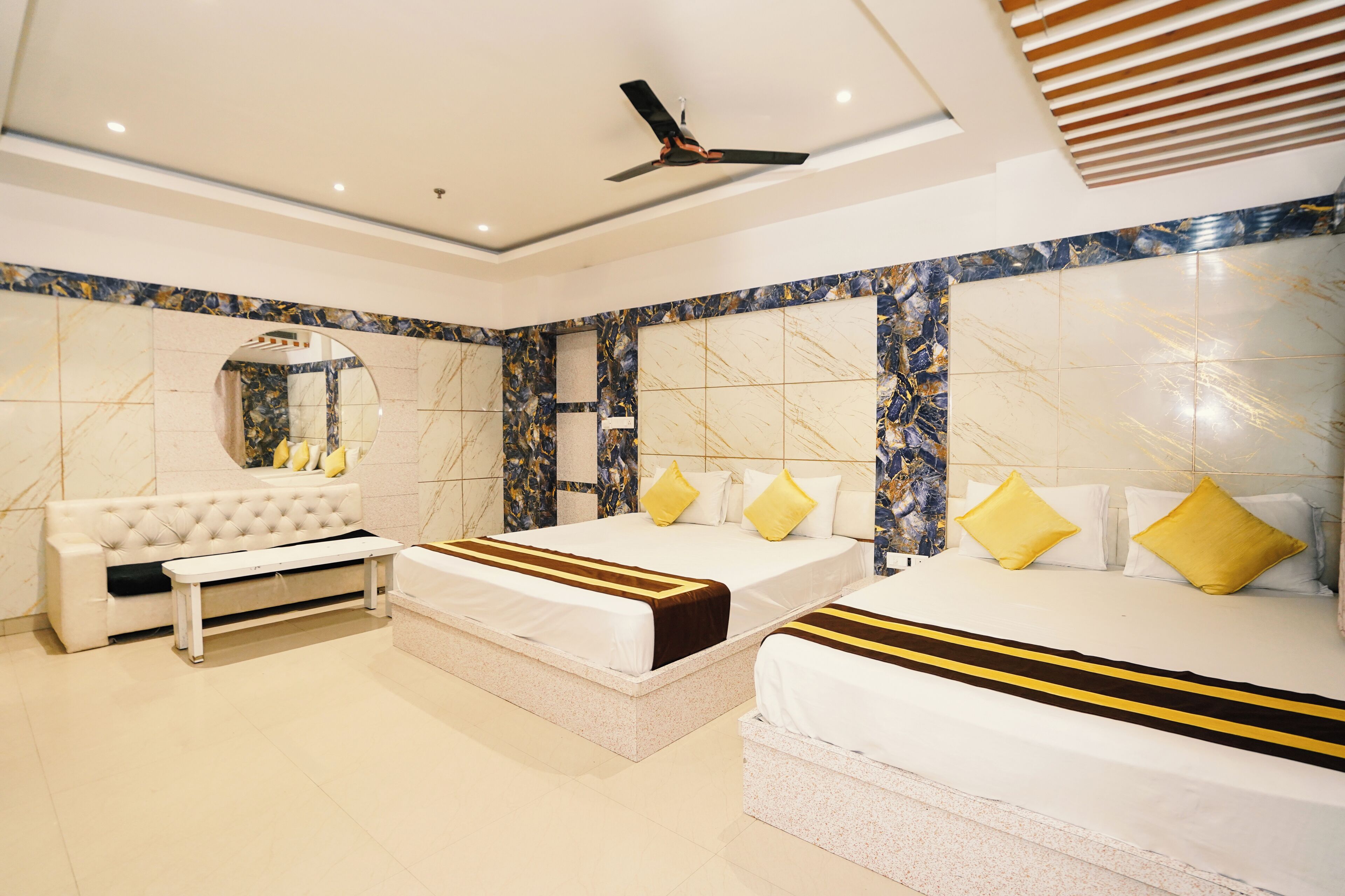A modern hotel room with two beds, a sofa, a bench, and a ceiling fan.