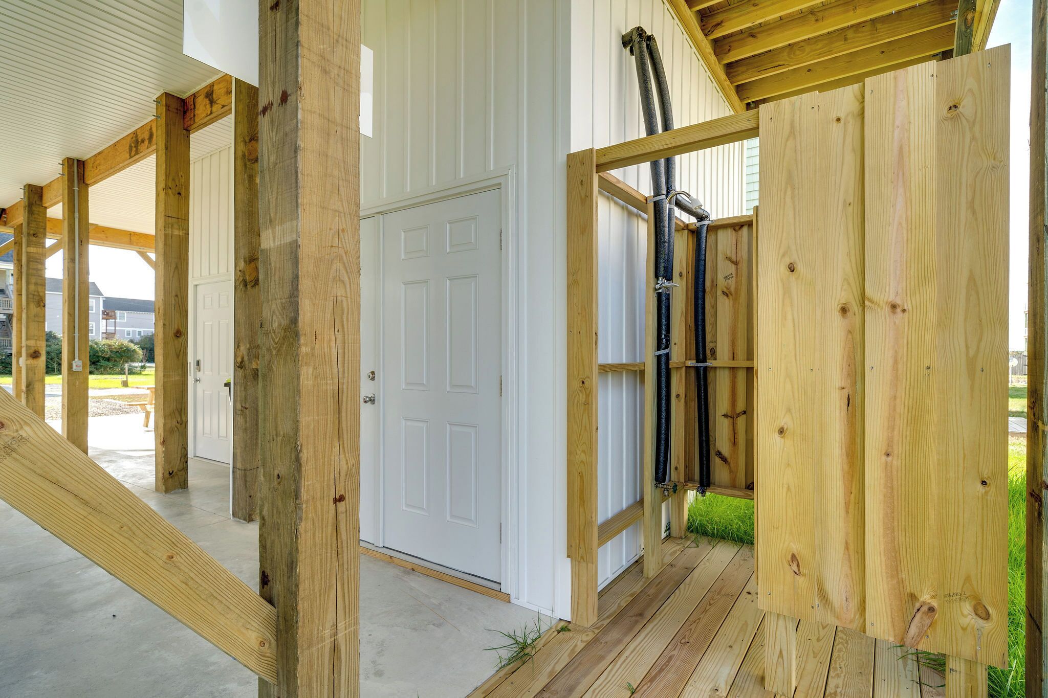 A wooden deck with a white door and a black hose running along the wall.