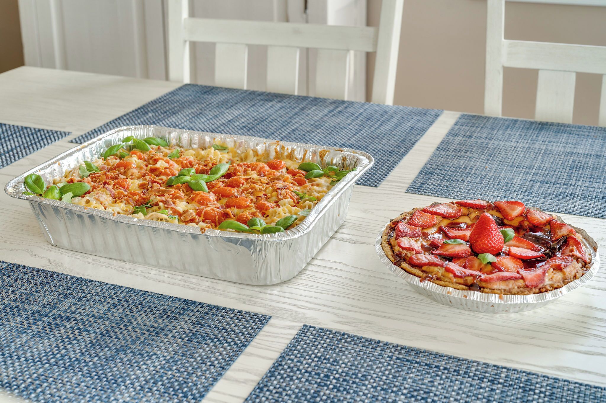 A rectangular aluminum tray with food on a blue and white checkered tablecloth.